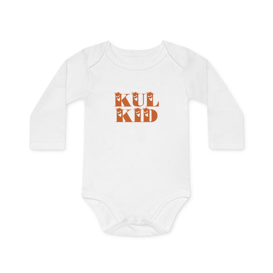 Baby iført hvit body med oransje trykk fra KUL KID, sittende på lys bakgrunn.